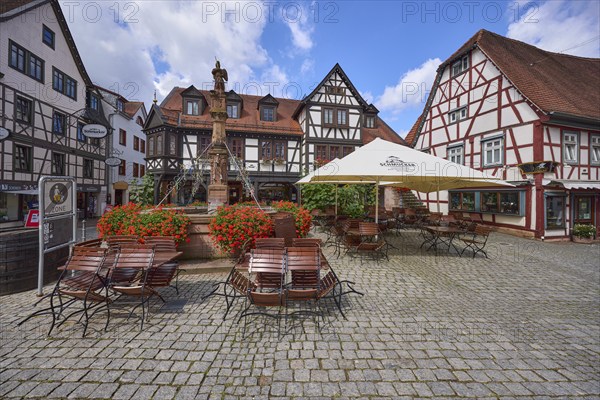 Market fountain with geraniums, half-timbered houses and outdoor areas of a restaurant with