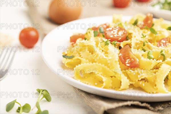 Reginelle semolina pasta with tomato, eggs, sesame and microgreen sprouts on a white wooden