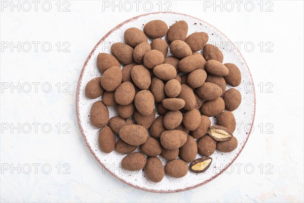 Almond in chocolate dragees on ceramic plate on white concrete background. Top view, close up, flat