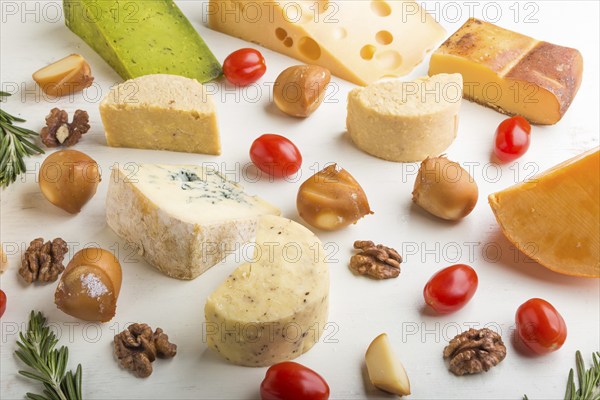 Set of different types of cheese with rosemary and tomatoes on a white wooden background. Side