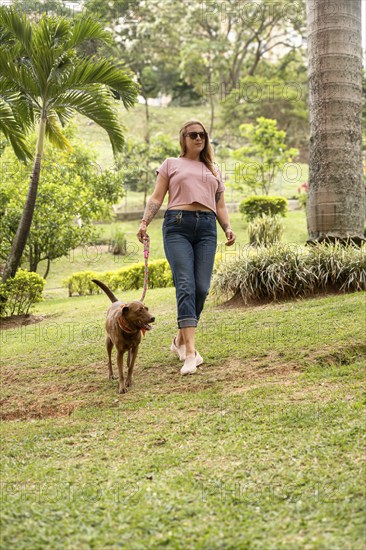 Vertical shot of a happy woman walking on the grass with her pet beside her outdoors. The woman is
