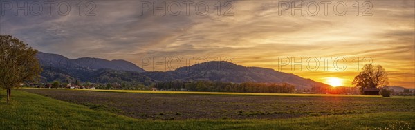 Sunset over a wide landscape with fields and mountains in the background, pastel-coloured sky and