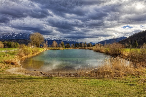 An idyllic pond against a mountain backdrop with a dramatic cloudy sky and autumnal vegetation,
