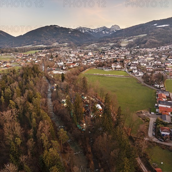 View of a village with a river and snow-capped mountains in the background, surrounded by green