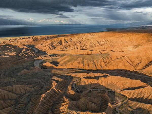 Riverbed runs through a landscape of eroded hills, badlands at sunset, Issyk Kul Lake in the
