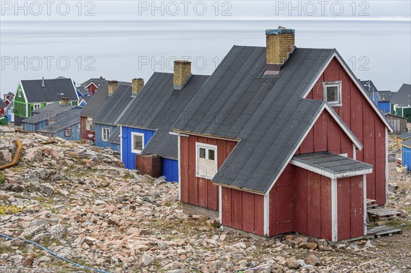 Colourful houses with black roofs stand on rocky ground near a grey coastline, fjord, remote Arctic