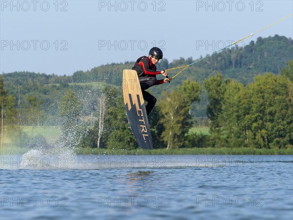 Young man jumping with wakeboard in lake, water sports, water skiing in wakepark, Stráž pod