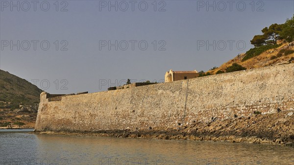 Long, old stone wall along the coastline, surrounded by a hill and calm sea, Venetian Sea Fortress,
