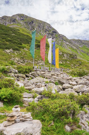 Scene in the mountains with colourful flags, a sign and green vegetation, surrounded by rocks,