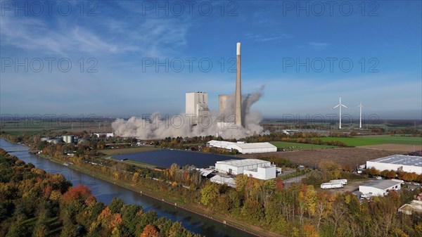 A power plant is being demolished, smoke rises, wind turbines stand next to it in an autumn