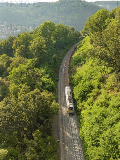 Train on railway tracks between dense trees and wooded hills, track construction, rail delivery for