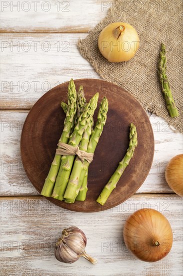 Bunch of fresh green asparagus, garlic, onion on white wooden background. Top view, flat lay, close