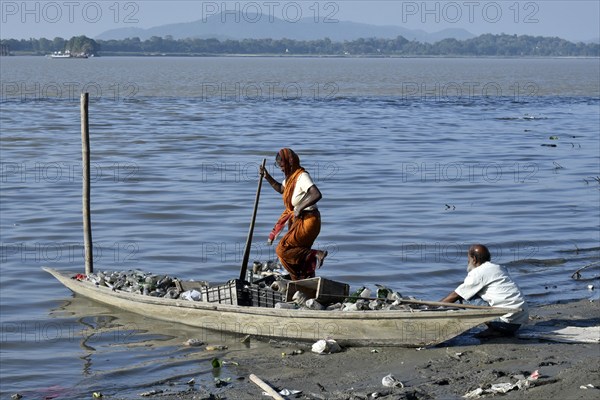 Rag picker collecting plastic bottle and other plastic materials in a boat from the bank of
