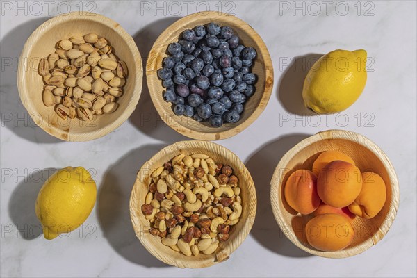 Healthy food, lemons, nuts, blueberries, apricots and pistachios in wooden bowls, on a marble
