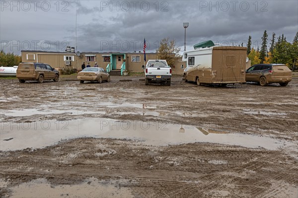 Dirty cars and muddy car park in front of pub, adventure tourism, Dalton Highway, Alaska, USA,