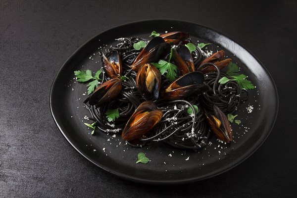 Spaghetti with black squid, black pasta, with boiled mussels, on a black plate, with parsley and