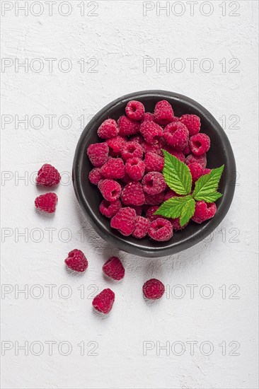 Fresh raspberries, on a black plate, with leaves, top view, on a white table