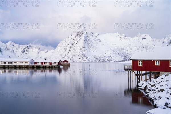 Rorbuer huts of Hamnoy at the fjord, snowy mountains in the background, Hamnøy, Reine, Moskenesøya,