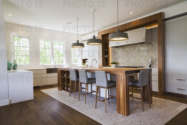 Walnut wood island with grey leather and wooden high chairs on travertine mosaic floor surrounded