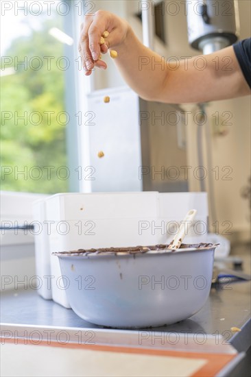 Hand sprinkles nuts into a bowl coated with dark chocolate, Burch Schokolade production,
