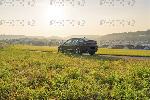 SUV driving through a wide landscape with a village and hills in the evening sun, VW ID5 electric