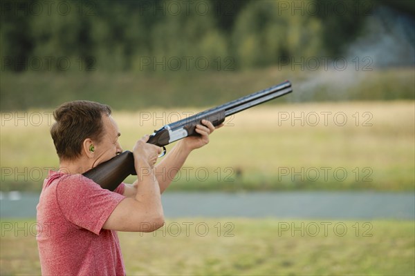 An old man shoots from a hunting rifle at a shooting range. Smoke from the barrel is visible in the