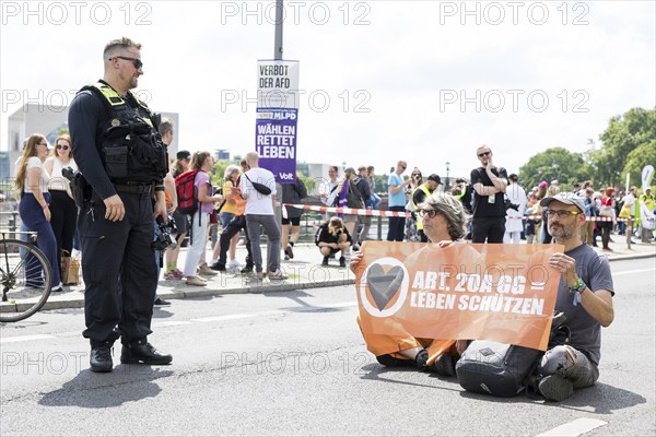 A police officer observes two Last Generation activists with a banner on Article 20A of the Basic