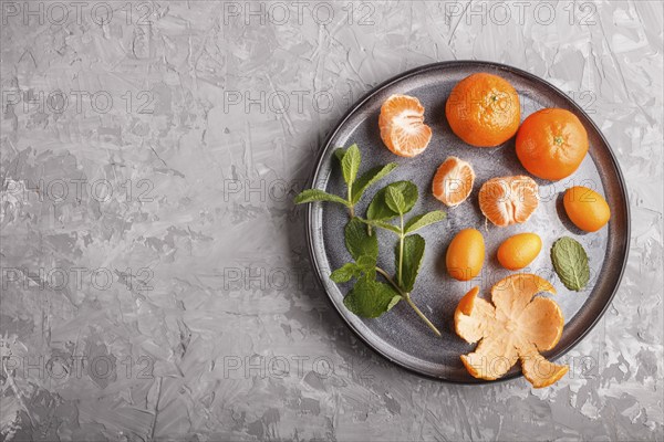 Tangerines, kumquats and a branch of mint on ceramic plate on a gray concrete background, top view,