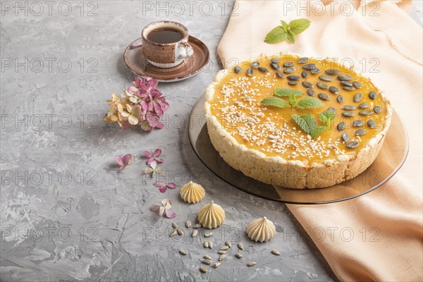 Traditional american sweet pumpkin pie decorated with mint, sesame and pumpkin seeds with cup of