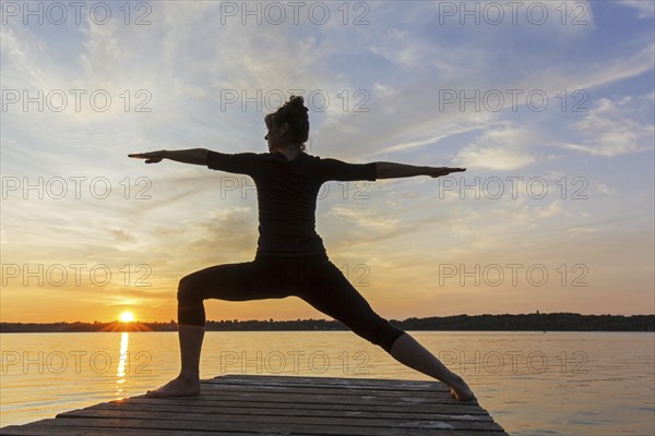 Woman practicing yoga posture Virabhadrasana II, Warrior Pose, lunging standing asana on jetty at