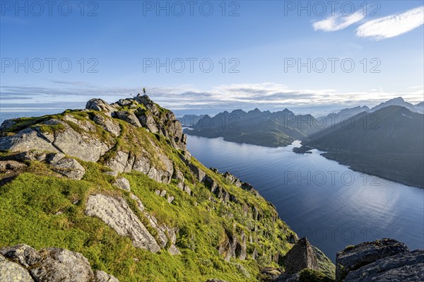 Climber on the summit of Dronningsvarden or Stortinden, behind sea and fjord Umvågsundet,