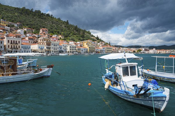 Harbour town with boats in the foreground and a forested range of hills in the background under a