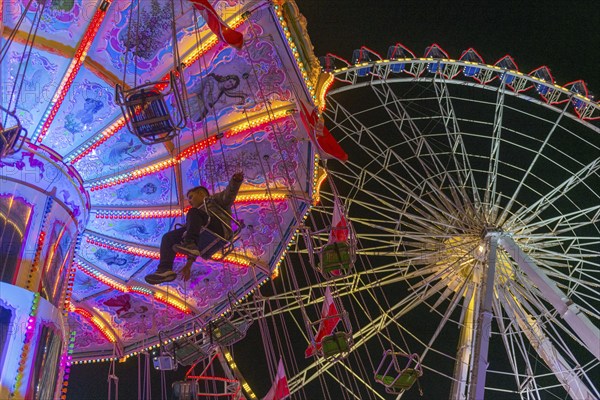A funfair at dusk with illuminated chain carousel and Ferris wheel, Europa Rad, rides, wave flight,
