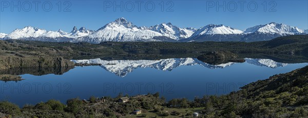 The snow-covered Mt. Cerro Castillo is reflected in a lake, small farm by the lake, Panorama,