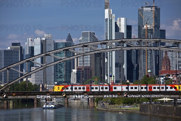 Main with regional railway on the Deutschherrnbrücke and a cargo ship in front of the skyline of