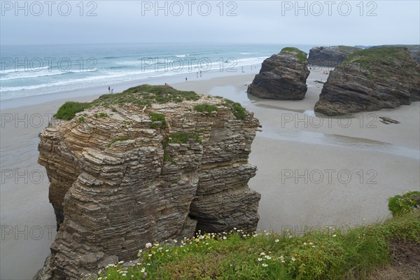 Huge rocks on the beach overlooking the sea. People walking along the shore under a cloudy sky,