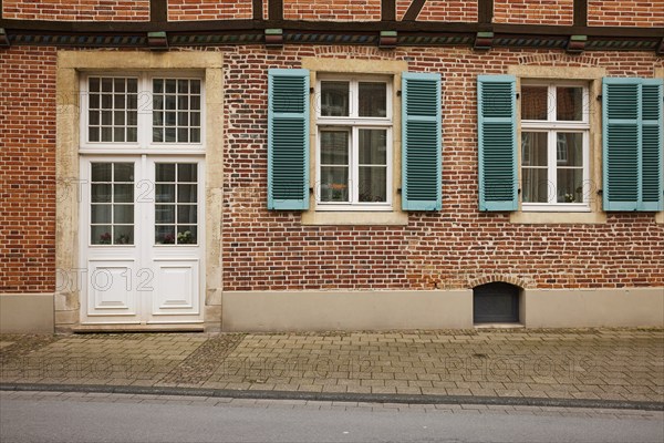 White entrance door and windows with blue-green shutters on a brick house in Warendorf, Warendorf