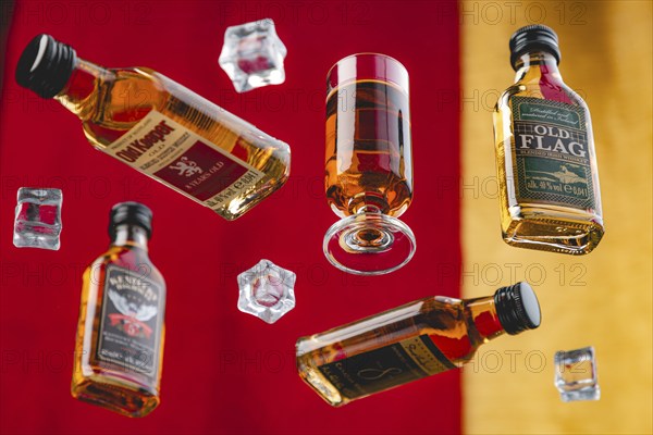 Four whisky bottles and a glass of whisky between floating ice cube cubes against a yellow and red