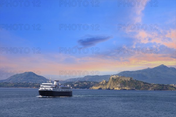 Italy, scenic sunset over Procida Island near Naples with boat approaching it from afar, Europe