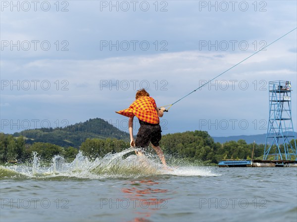 Man with red hair and flapping shirt on wakeboard, water ski and wakepark, Stráž pod Ralskem, Czech