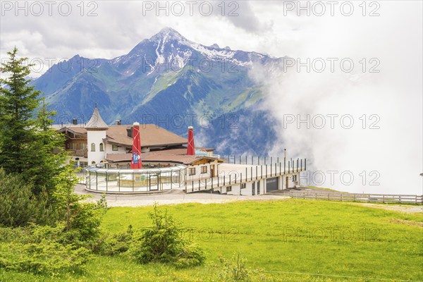 A building on a hill in front of a mountain backdrop with clouds and a green meadow, quiet and