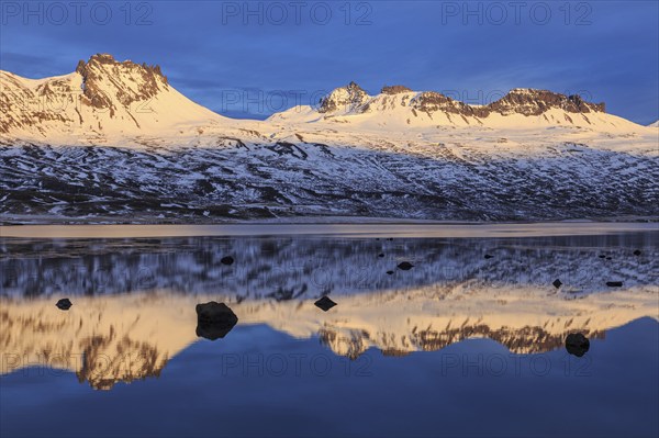 Snow-covered mountains reflected in a fjord in the evening light, Berufjördur, East Fjords,