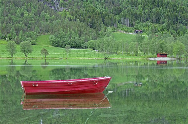 A small red boat floats on a calm lake with green surroundings, Stryn, Mindesundet, Fjordland,
