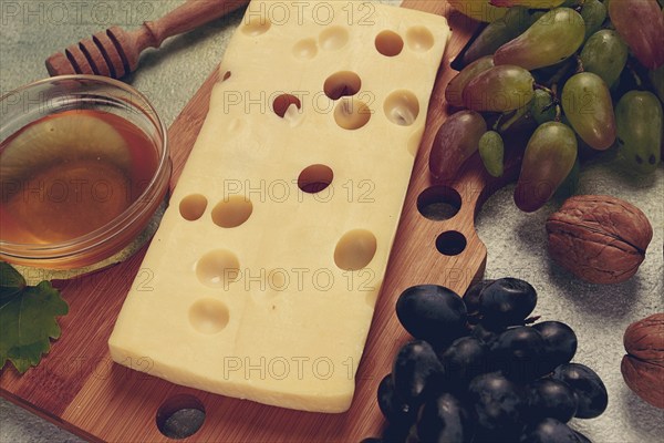 Cheese with big holes, emmental, maasdam, brie cheese, on a cutting board, with grapes and honey,