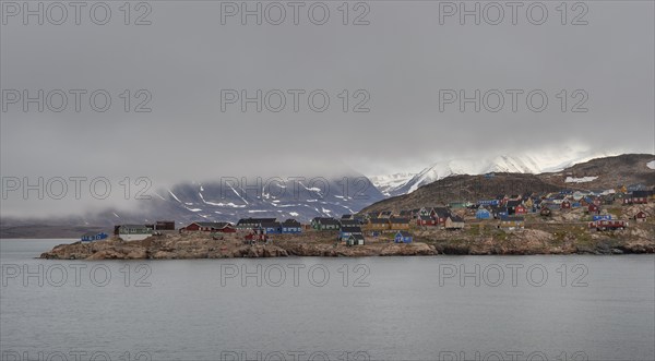 Colourful houses, secluded Arctic Inuit settlement, cloudy coastal landscape against a mountain