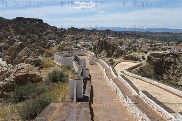 Panoramic view of a mountainous landscape with winding paths and a wide horizon under a summer sky,