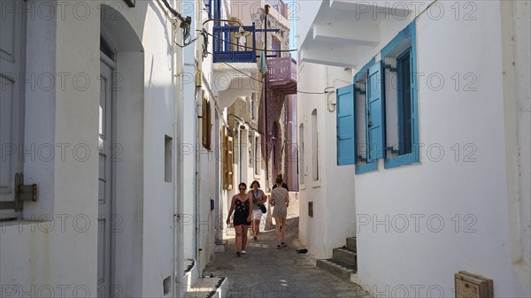 Narrow alley with white walls and colourful shutters, strollers in summer, Mandraki, Nisyros,