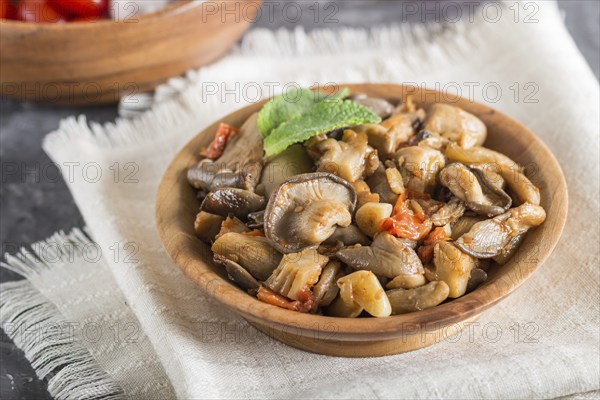 Fried oyster mushrooms with tomatoes in wooden plate on black concrete background. side view, close