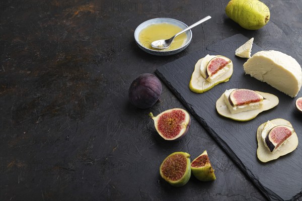Summer appetizer with pear, cottage cheese, figs and honey on slate board on a black concrete