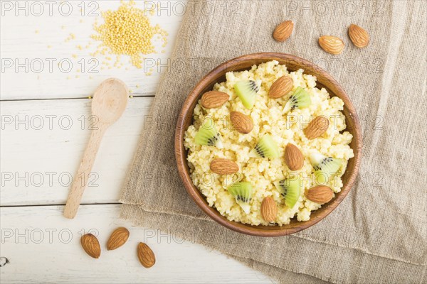 Millet porridge with kiwi and almonds in wooden bowl on a white wooden background and linen textile